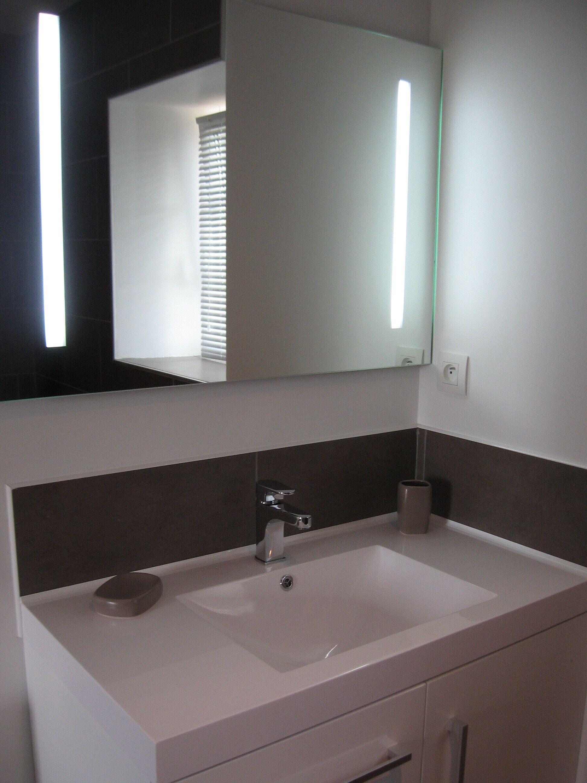 Un baño con lavamanos blanco, un espejo y un perchero para toallas.