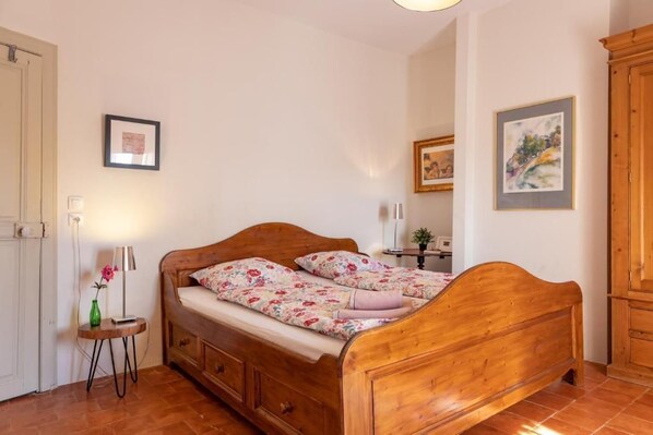 Un dormitorio con una cama de madera, una mesita de noche con una lámpara y un pequeño florero verde.