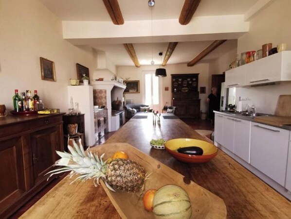 A spacious kitchen with wooden flooring, a long counter, and a variety of fruits and vegetables. - Maison du Lavoir Vert (Tourbes)