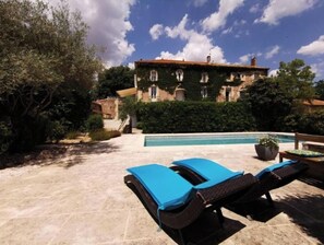 Zona junto a la piscina con sillones de descanso y vistas a un edificio con muros cubiertos de hiedra.