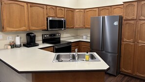 A kitchen with wooden cabinets, a stainless steel refrigerator, a microwave, an oven, a coffee maker, and a sink. - Sun Lakes Country Club (Sun Lakes)