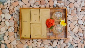 A wooden tray with a dental kit, sanitary bag, comb, and shower cap on a bed of pebbles. - The MG Villa & SPA (Penida Island)