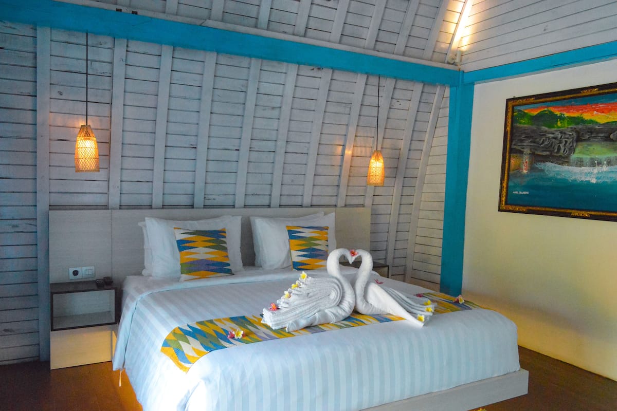 A hotel room with a bed, pillows, a nightstand, and a painting on the wall.