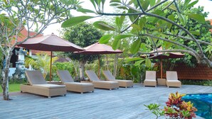 A wooden deck with lounge chairs and umbrellas, a swimming pool, and lush greenery. - The MG Villa & SPA (Penida Island)
