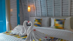 A hotel room with a bed featuring two swan-shaped towels, a striped bedspread, and a wall-mounted light fixture. - The MG Villa & SPA (Penida Island)