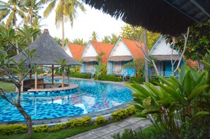A pool surrounded by thatched-roof cottages, lush greenery, and a clear blue sky. - The MG Villa & SPA (Penida Island)
