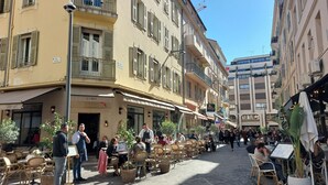 Een geplaveid straatje met cafés en restaurants, met terrasjes en traditionele Europese architectuur.