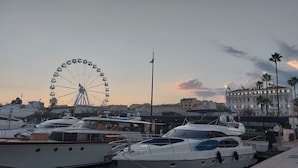 Een jachthaven met aangemeerde jachten, een reuzenrad op de achtergrond en een gebouw met de aanduiding 'SPLENI'.