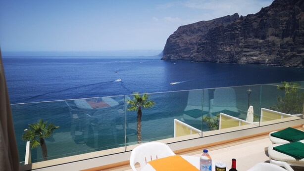 Un balcone con vista sul mare e su una scogliera, con un tavolo su cui si trovano una bottiglia di vino, una bottiglia d'acqua e un vassoio di snack.