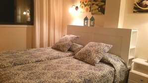 Un letto con biancheria a motivi, due cuscini, un comodino e lanterne a parete.