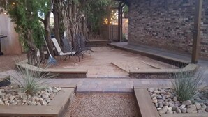 An outdoor patio area with a brick wall, a pergola with chairs, and a gravel pathway. - The Aoudad Cabin at Palo Duro  (Canyon)