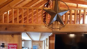 A wooden interior with a star-shaped light fixture, a welcome sign, a kitchen area, and a TV mounted on the wall. - The Aoudad Cabin at Palo Duro  (Canyon)
