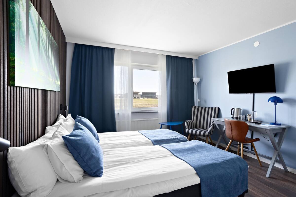 A hotel room with a bed, a desk, a chair, a television, and a window with curtains.