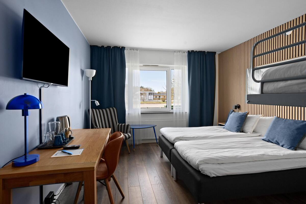 A hotel room with a bed, desk, chair, TV, and a window with curtains.