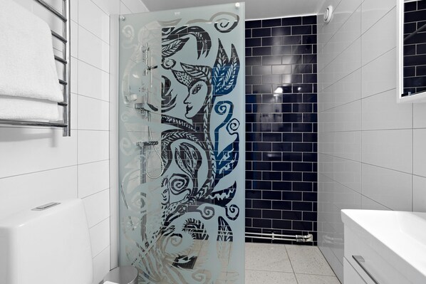 Une salle de bain avec une baignoire blanche, une cabine de douche en verre ornée d’un motif décoratif et un mur recouvert de carreaux noirs.