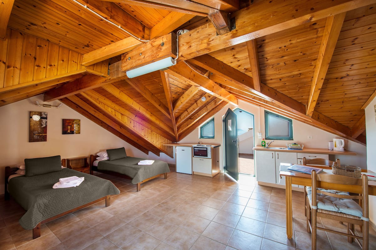 A cozy attic bedroom with two beds, a kitchenette, and a dining area.