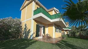 A two-story building with a balcony, a small patio with outdoor furniture, and lush greenery. - Theros Retreat (Kefalonia)