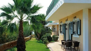 A building with a patio area featuring a palm tree, a brick pathway, and outdoor seating. - Theros Retreat (Kefalonia)