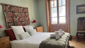 Un letto rifatto con cura, con una coperta verde, due comodini in legno, una lampada rossa e una grande libreria piena di libri e oggetti decorativi.