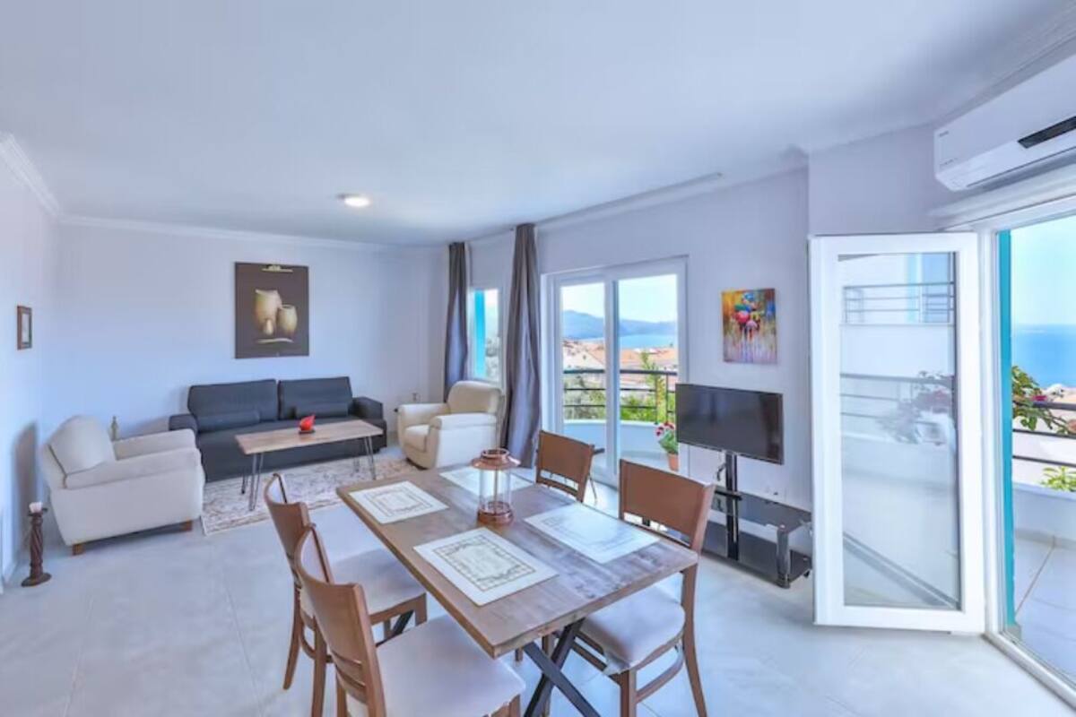 Una sala moderna con sofá, mesa de comedor, sillas, televisor y un balcón con vistas.