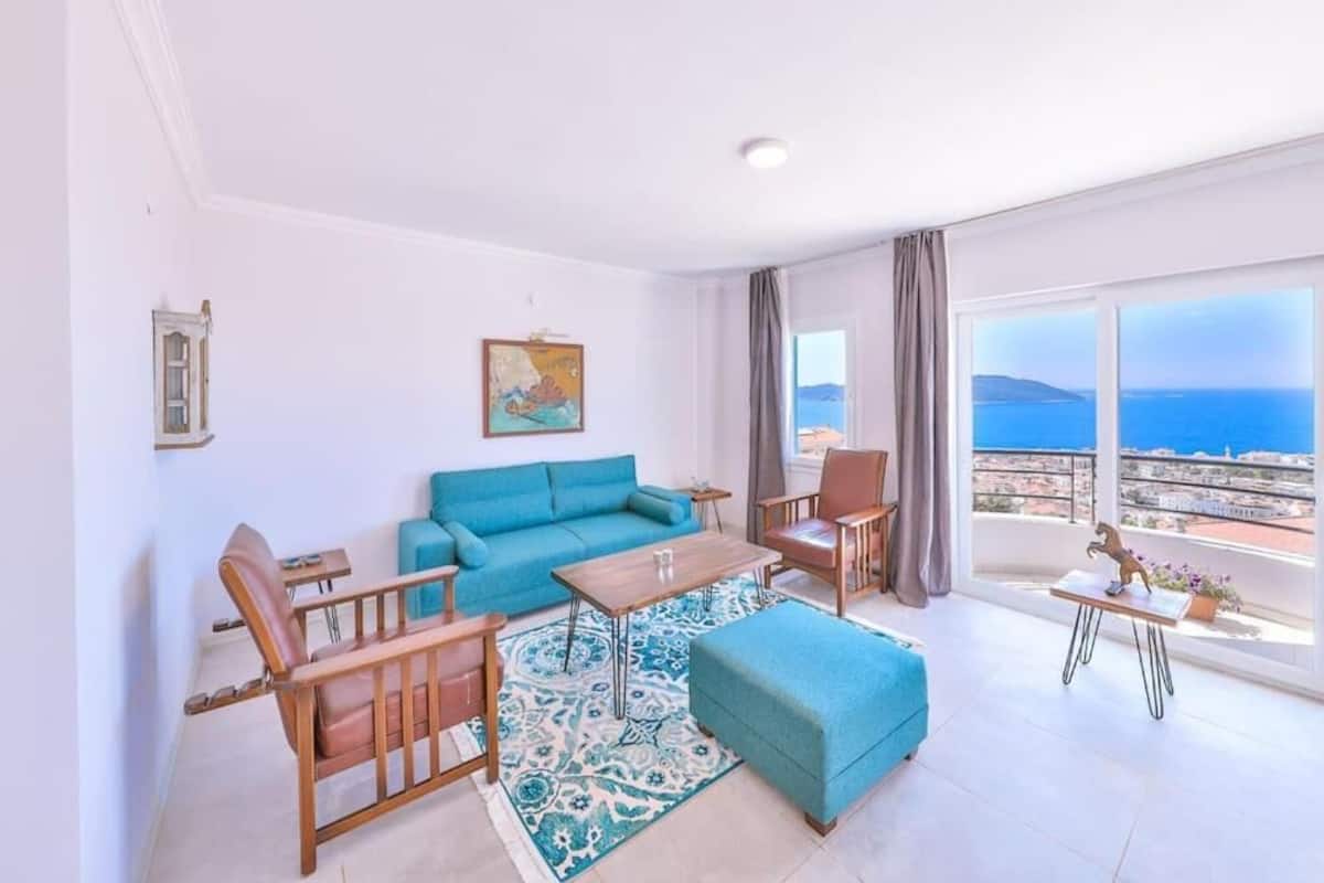 Una sala de estar moderna con un sofá azul, sillones de madera, una mesa de centro y vista al mar.