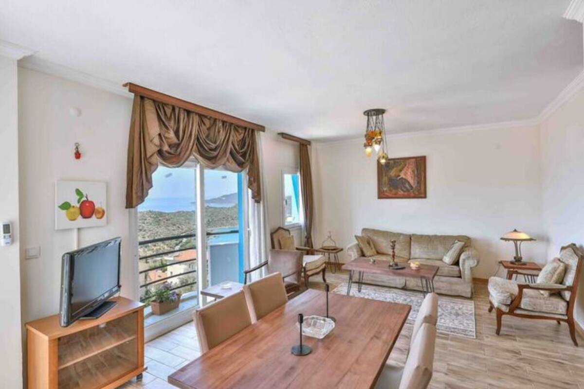 Una sala de estar con una mesa de comedor de madera, sofás, televisor y un balcón con vistas.