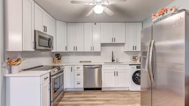 A modern kitchen with white cabinets, stainless steel appliances, a ceiling fan, and a wooden floor. - Newly Remodeled Condo - Steps to Beach & Boardwalk (Ocean City)