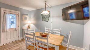 A dining room with a wooden table and white chairs, a hanging lamp, and a television mounted on the wall. - Newly Remodeled Condo - Steps to Beach & Boardwalk (Ocean City)