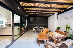 An outdoor patio with a wooden table and chairs, a sofa, and a dining table with chairs.