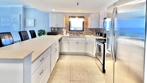A modern kitchen with white cabinets, a large island, stainless steel appliances, and a view of the ocean. - Beach Front,2bed 2bath, Pool, Huge Balcony (panama city beach)