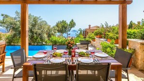 Un espace repas offrant une vue sur une piscine et des montagnes, avec des tables et des chaises en bois.