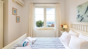 Une chambre d’hôtel avec un lit, une fenêtre avec des rideaux, un climatiseur fixé au mur et un tableau encadré.