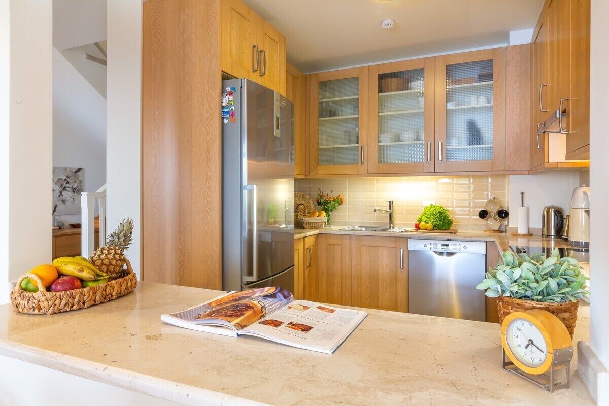 A modern kitchen with wooden cabinets, stainless steel appliances, and a fruit basket on the counter.