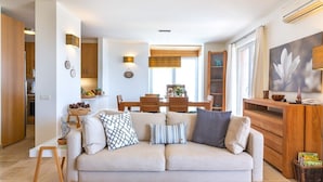 Un salon moderne avec un canapé beige, un coin repas doté de meubles en bois et une cuisine visible au fond.