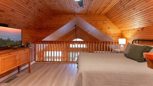 A cozy, wooden-paneled bedroom with a bed, a TV, and a balcony. - Incredible Mountain Views Near Dtown Gatlinburg! (Gatlinburg)