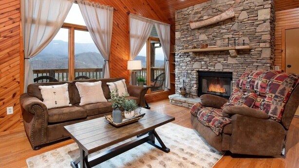 A cozy living room with a stone fireplace, wooden walls, and a view of the mountains. - Incredible Mountain Views Near Dtown Gatlinburg! (Gatlinburg)