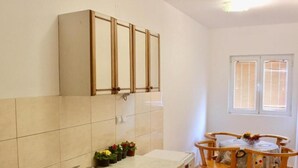 A compact kitchen with a sink, stove, and cabinets. There is a dining area with two wooden chairs and a table. - NIR Apartments Budva  (Budva)
