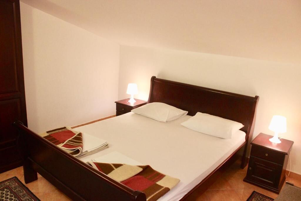 A neatly made bed with a white comforter and pillows, a wooden headboard, and two bedside tables with lamps.