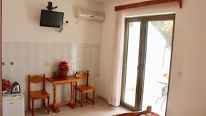 A compact room with a kitchenette, a wooden dining table with two chairs, a television mounted on the wall, and a sliding glass door leading to an outdoor area. - NIR Apartments Budva  (Budva)