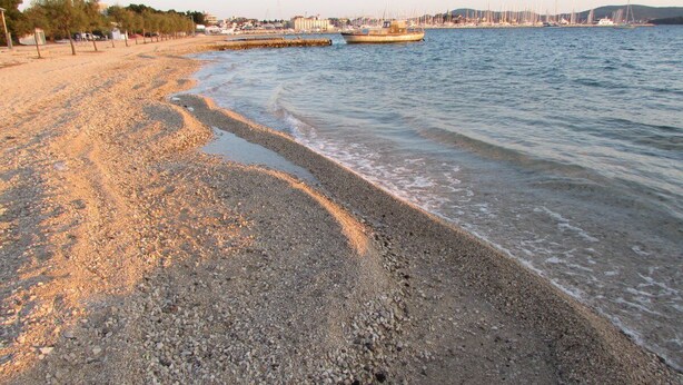 Una playa de guijarros con barcos al fondo.