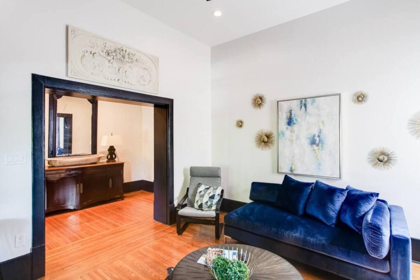 Un salon moderne avec un canapé bleu, une table basse et un fauteuil. Le sol est en bois et un miroir est accroché au mur.