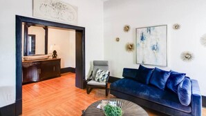 Una sala de estar moderna con un sofá azul, una mesa de centro y una silla. Hay piso de madera y un espejo en la pared.