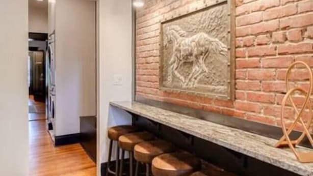 Zona de bar con pared de ladrillo, una escultura en la pared y taburetes.