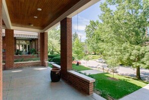 Un porche abrité, doté de colonnes en briques, d’un sol en béton et offrant une vue sur une rue résidentielle bordée d’arbres et où circulent des voitures.