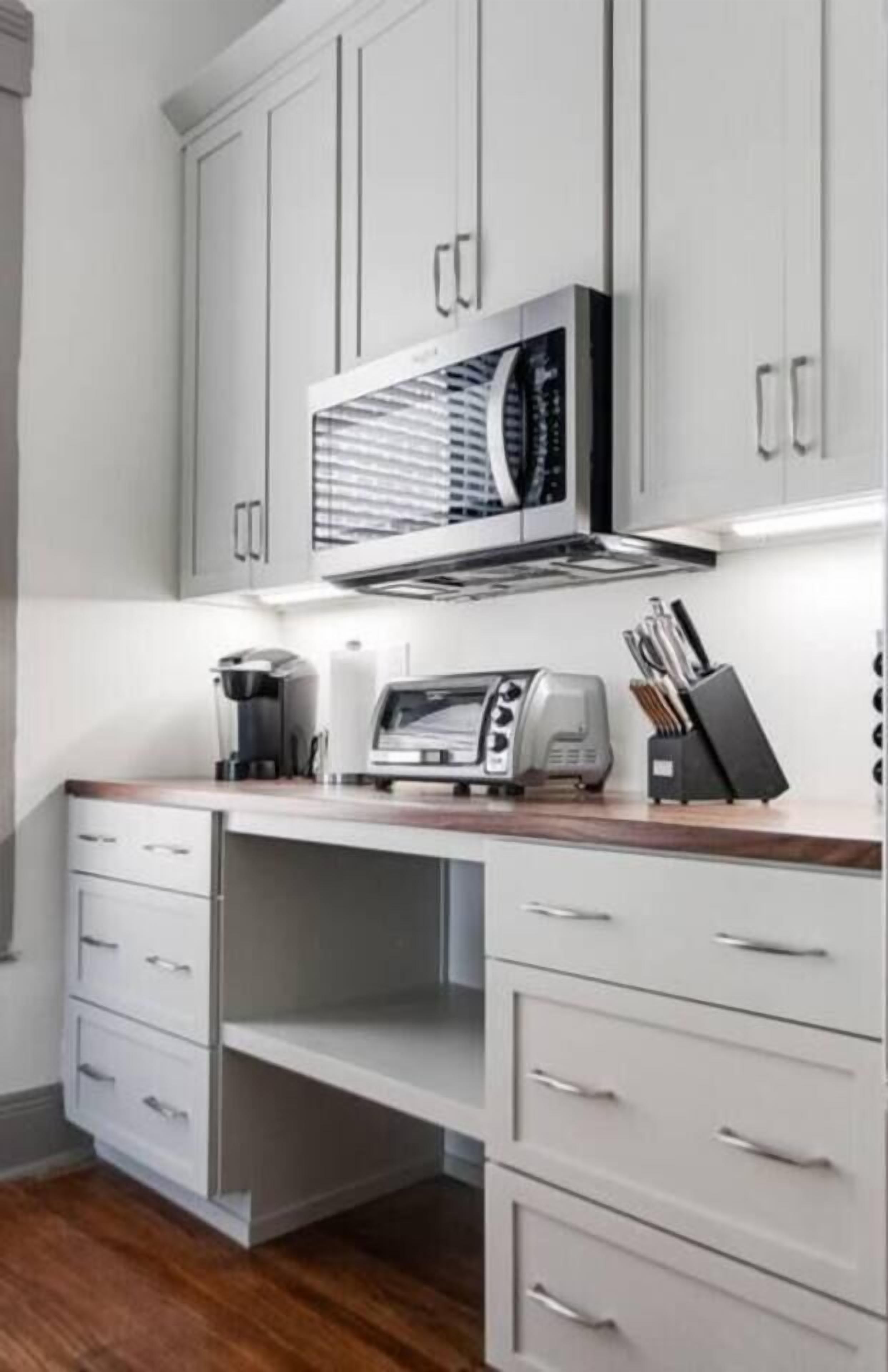 Eine moderne Küche mit weißen Schränken, einer eingebauten Mikrowelle, einer Kaffeemaschine und einem Toaster.