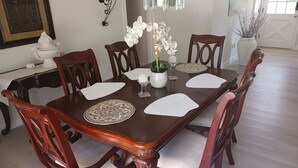 A dining table with six chairs, white placemats, a vase with white flowers, and a decorative wall piece. - Relax by the sea! Three bedroom home with pool awaits you near Destin Beaches. (Fort Walton Beach)