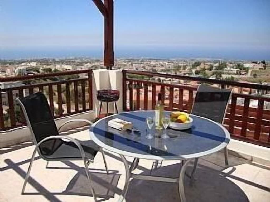 A balcony with a round glass table, two chairs, and a bottle of wine.