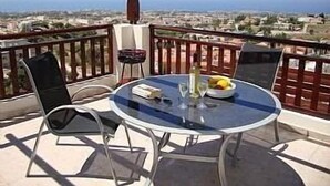 Un balcon avec une table ronde en verre, deux chaises et une bouteille de vin.
