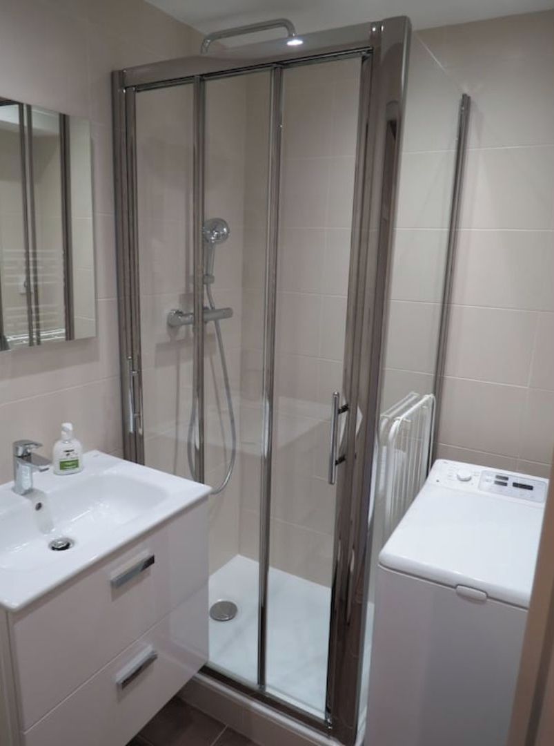 Une salle de bain moderne avec une douche à parois de verre, un lavabo blanc et un lave-linge encastré.