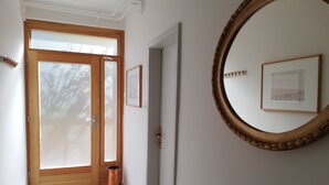 Ein Flur mit einer Holztür, einem Kupfer-Mülleimer und einem gerahmten Bild an der Wand.
